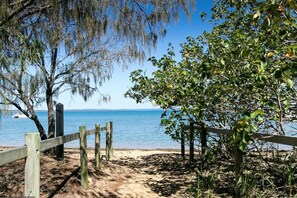 A beach with a wooden fence, trees, and a clear view of the water. - Boat Harbour Apartments (Urangan)