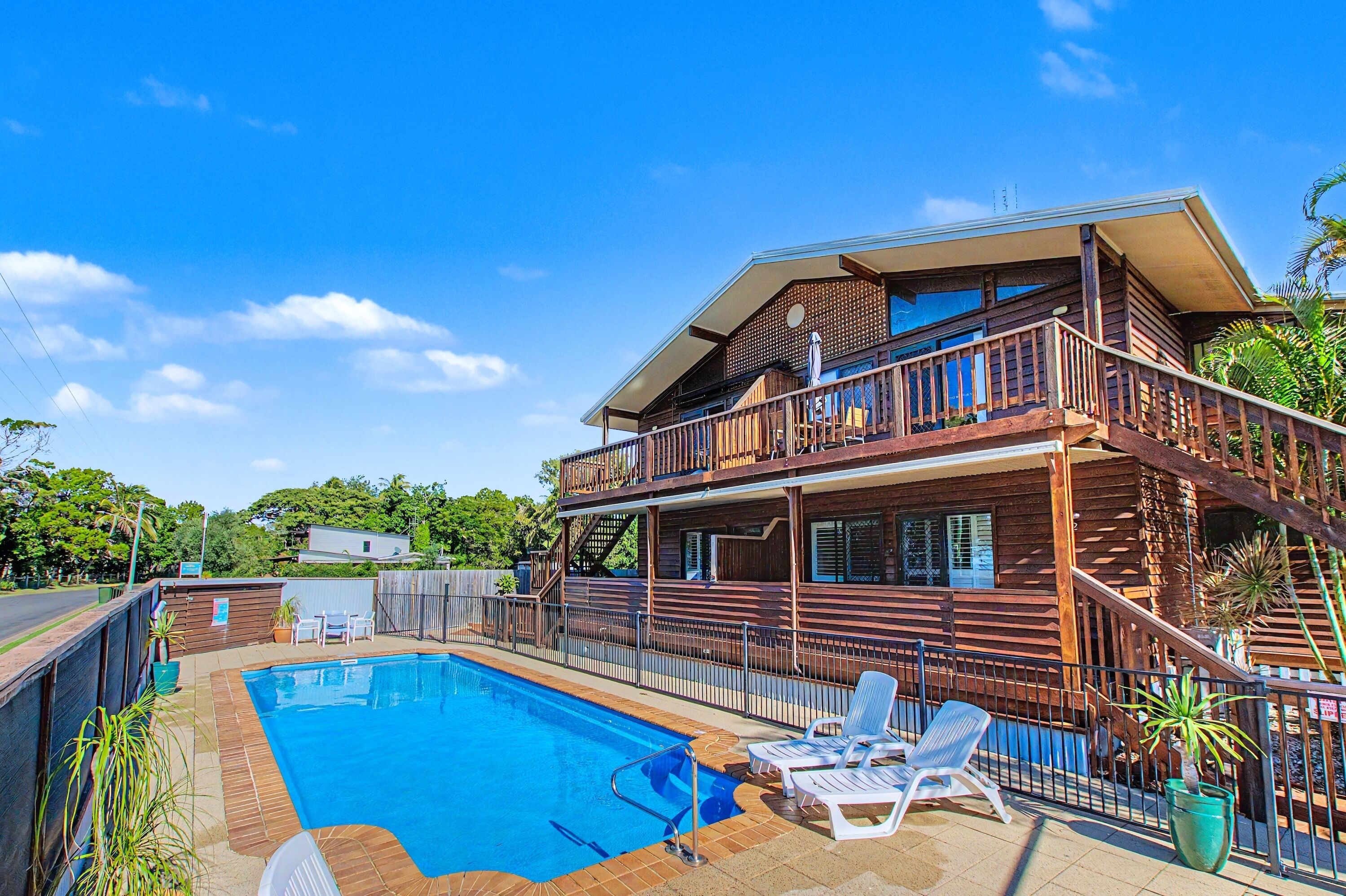 A two-story wooden house with a pool, lounge chairs, and a balcony.