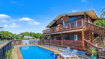 A two-story wooden house with a pool, lounge chairs, and a balcony.