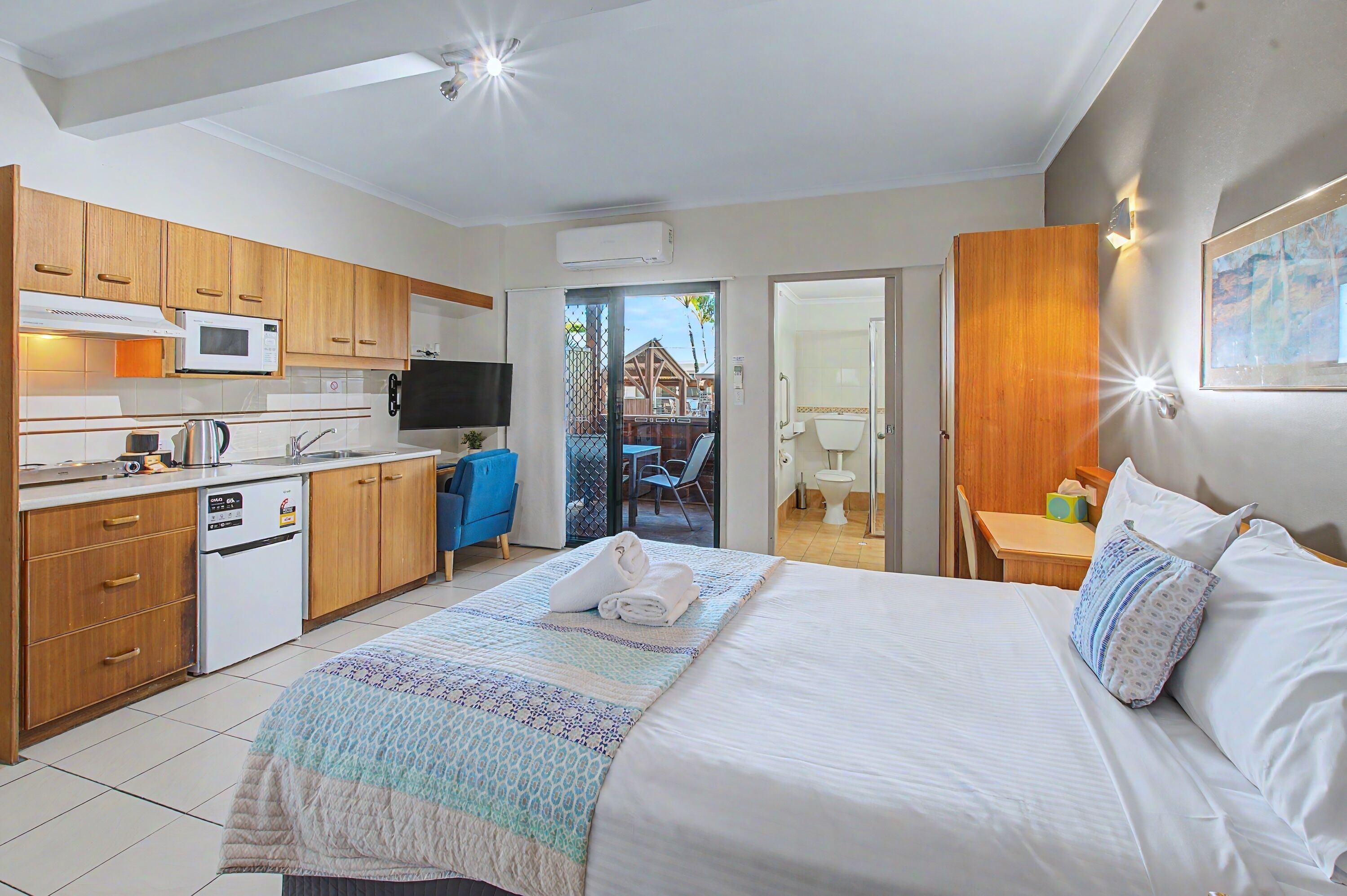 A hotel room with a bed, a kitchenette, a TV, and a view of the outside.