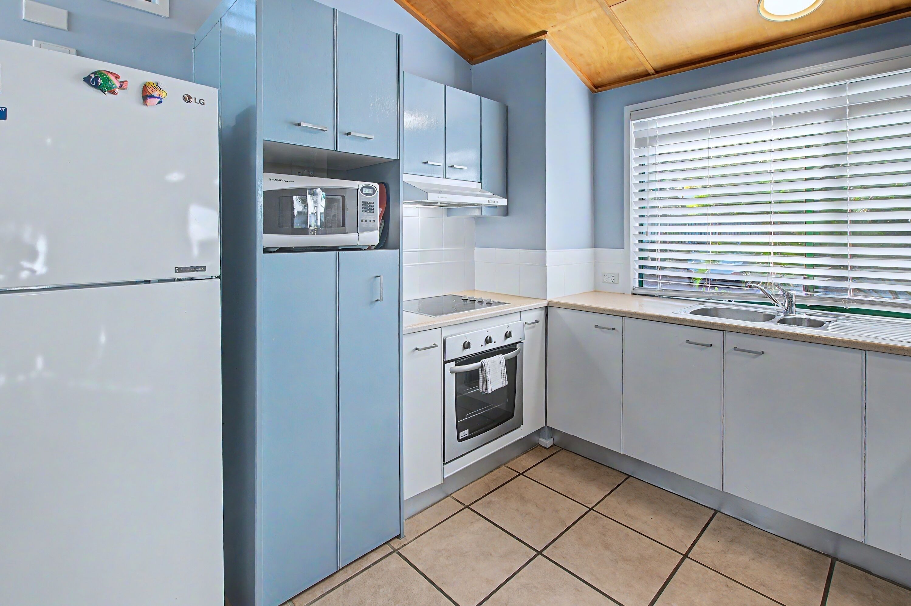Una cocina con un refrigerador blanco, microondas, estufa y pileta.