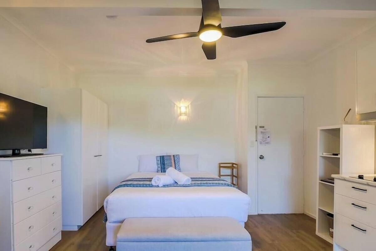 A bedroom with a bed, a TV, a ceiling fan, a bedside table, and a wardrobe.