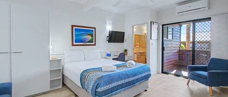 A hotel room with a bed, a ceiling fan, a TV, a sliding glass door to a balcony, and a blue chair.