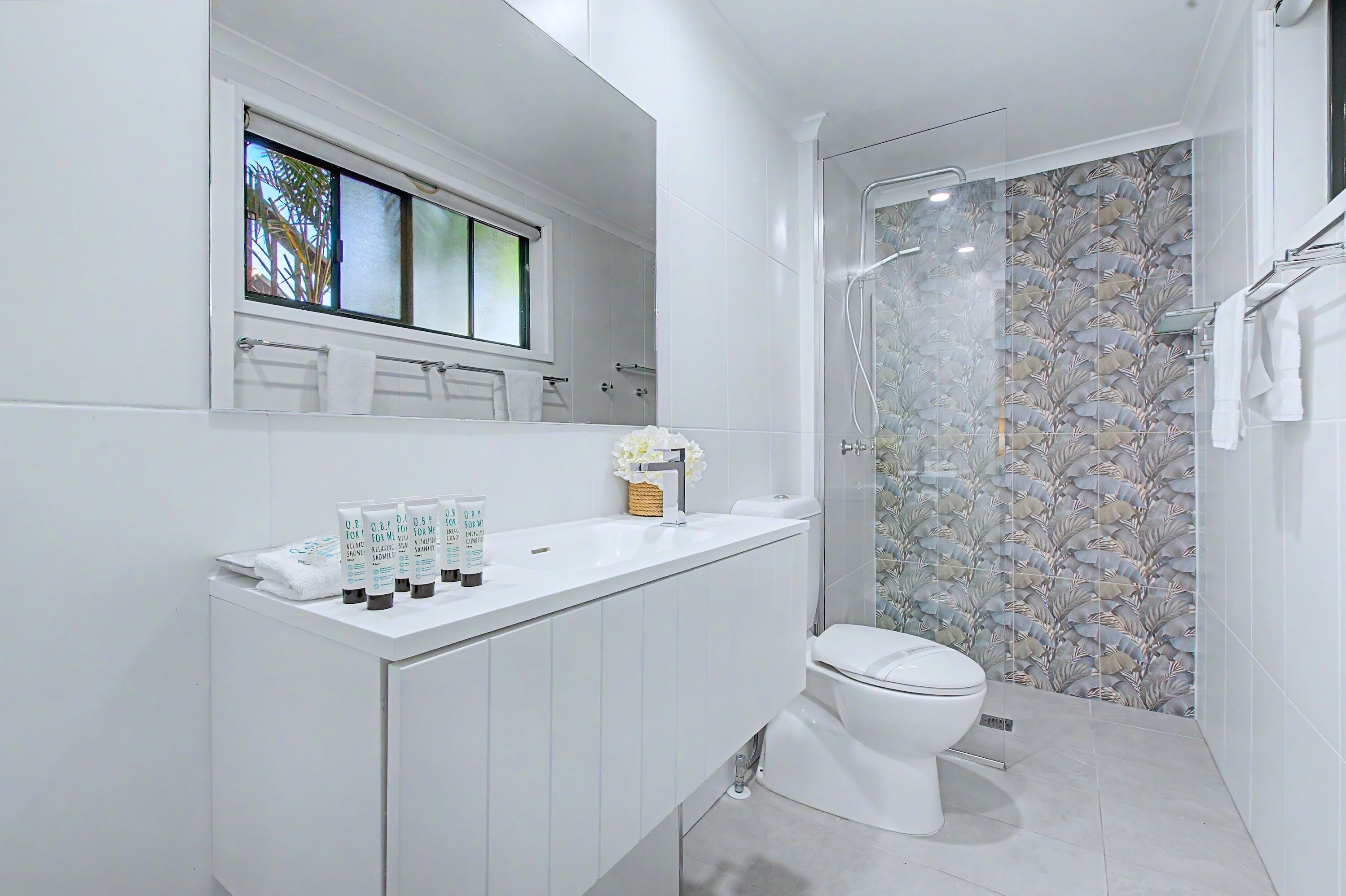 A modern bathroom with a toilet, a shower, and a vanity with toiletries.