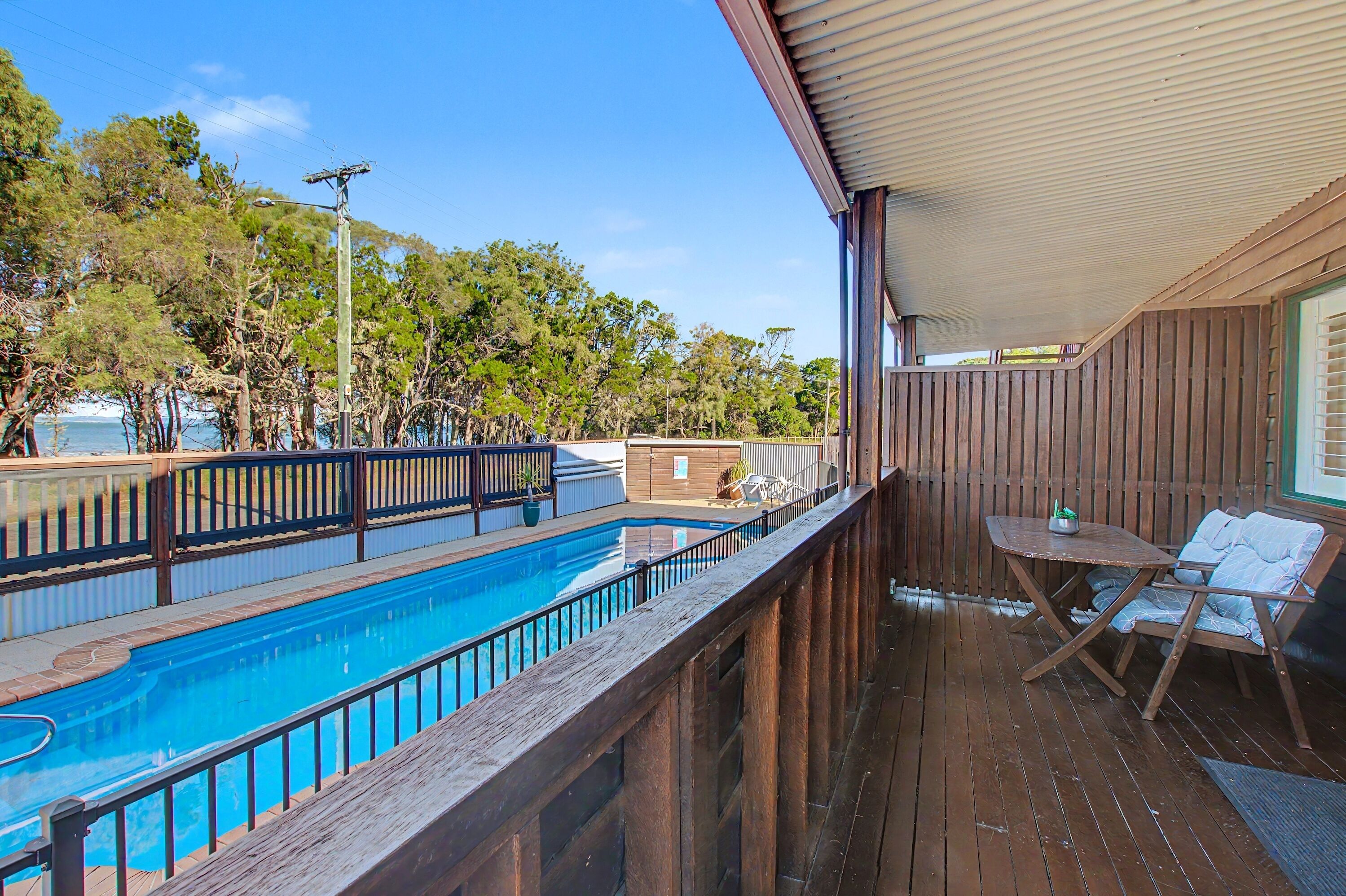Una terraza de madera con piscina, una mesa y una silla.