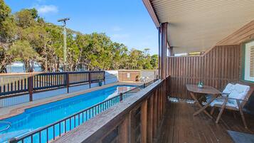 Una terraza de madera con piscina, una mesa y una silla.