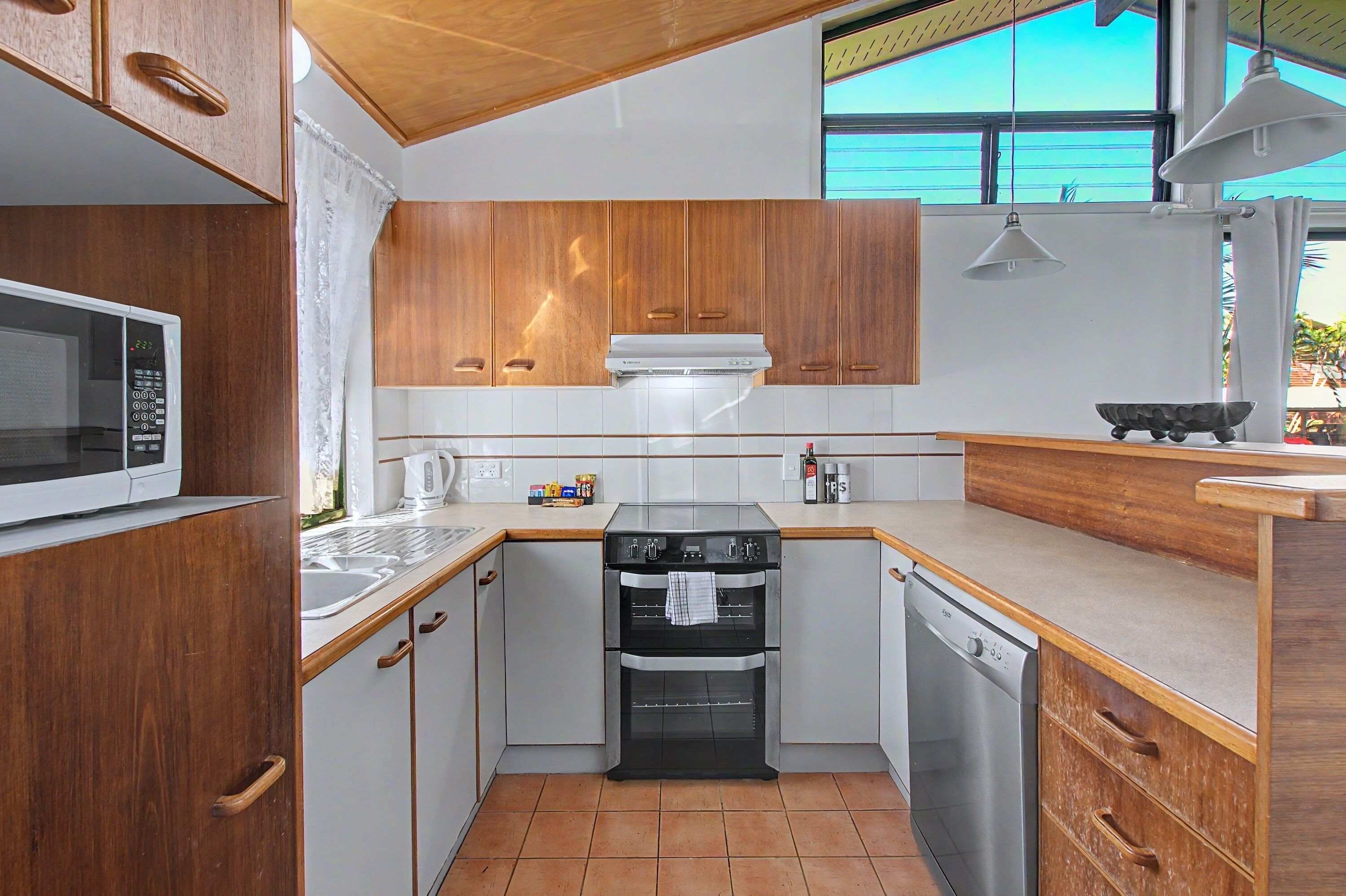 Cocina compacta con armarios de madera, microondas, horno y lavavajillas.