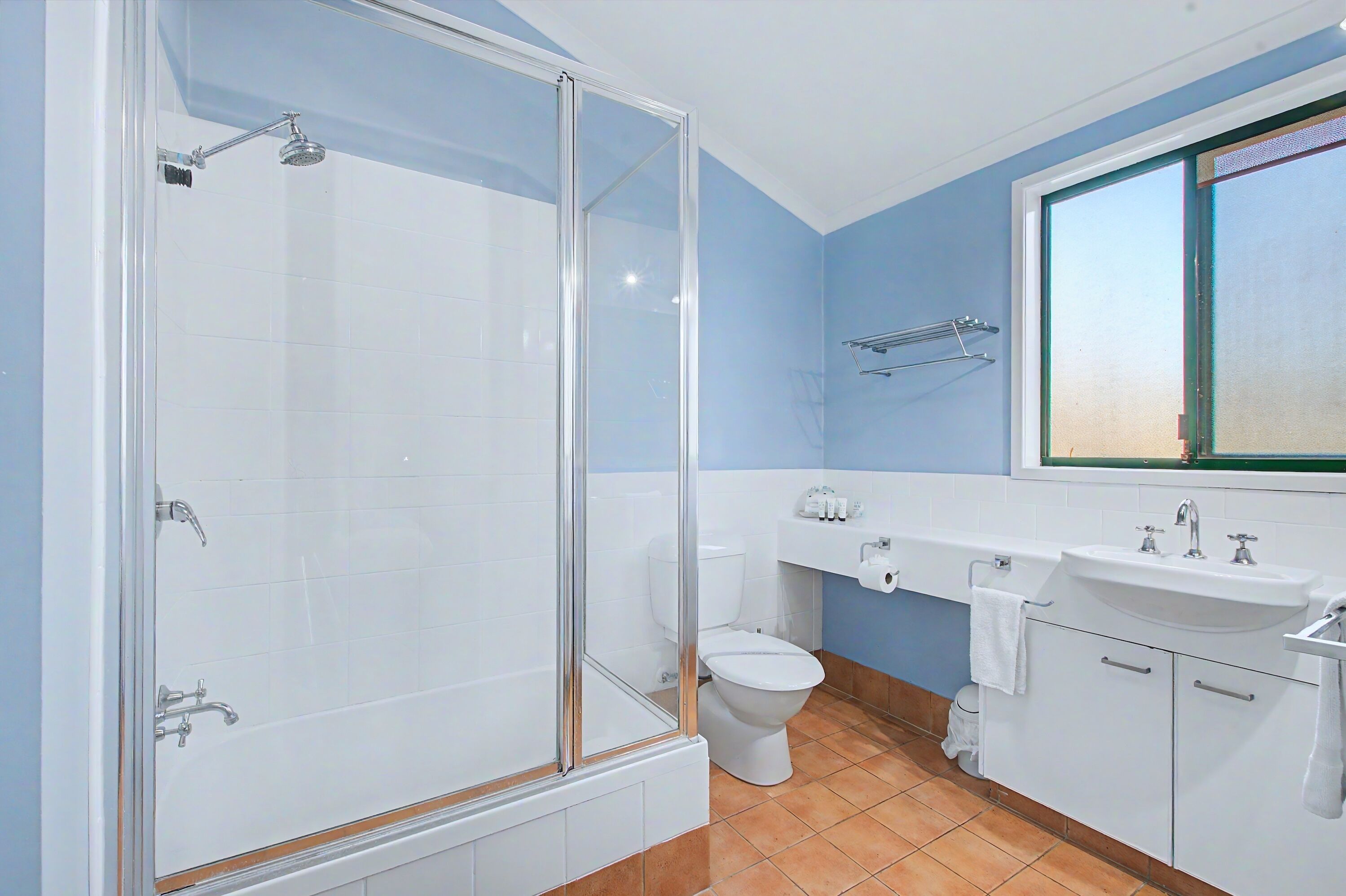 A bathroom with a glass-enclosed shower, a toilet, a sink, and a window.