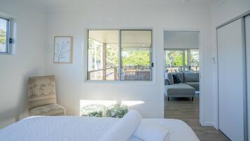 A bedroom with a large bed, a chair, a sofa, and a balcony with a view of trees.