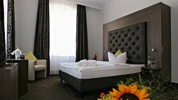 Una habitación de hotel con una cama grande, un escritorio, una silla y un ventanal con cortinas.
