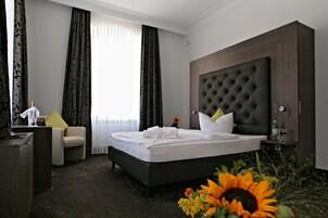 Una habitación de hotel con una cama grande, un escritorio, una silla y un ventanal con cortinas.