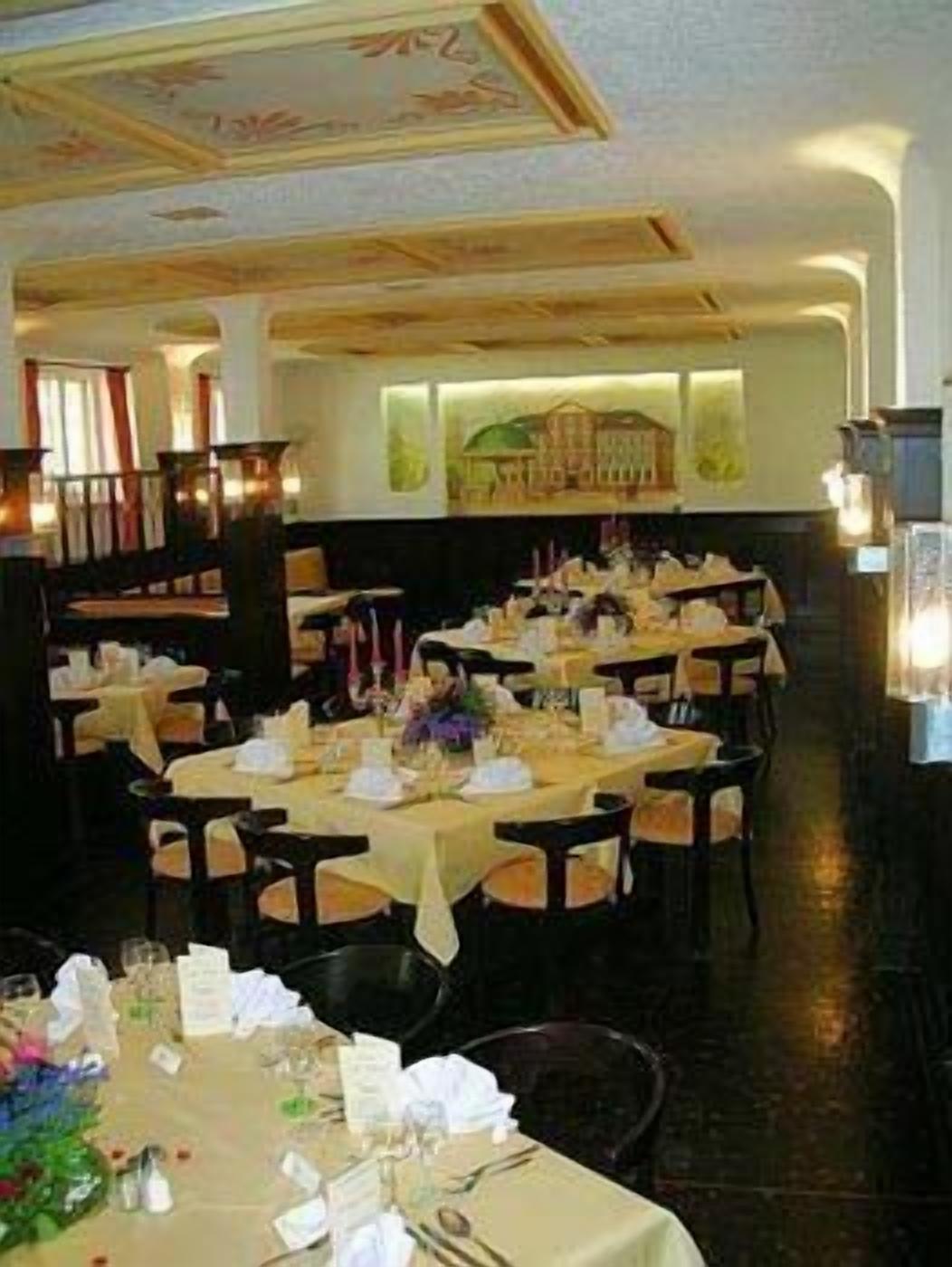 A formal dining room with multiple tables set for service, featuring a classic architectural design with a high ceiling and decorative moldings.