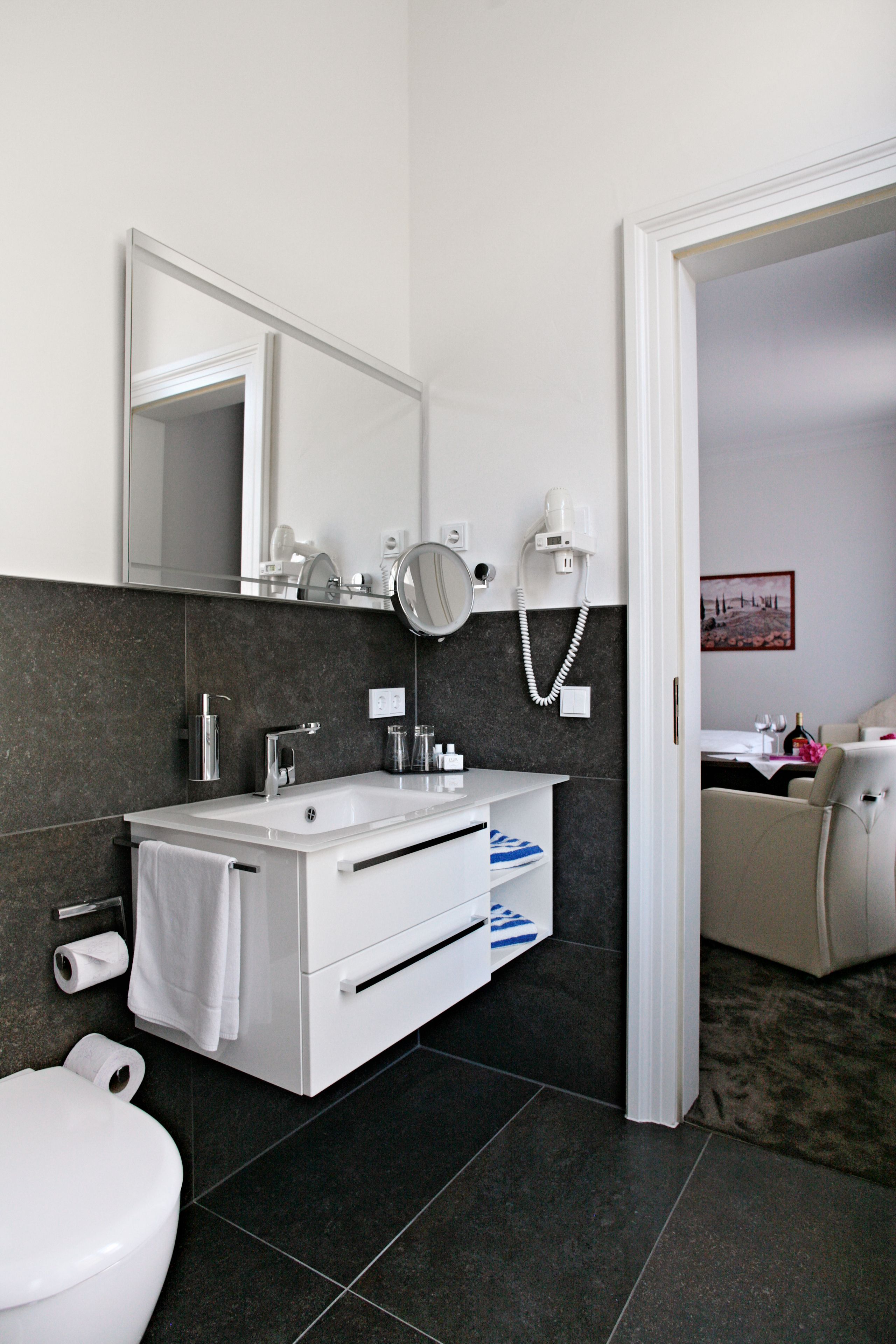 A modern bathroom with a white sink, dark tiles, a mirror, and a hairdryer.