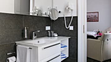 A modern bathroom with a white sink, dark tiles, a mirror, and a hairdryer.