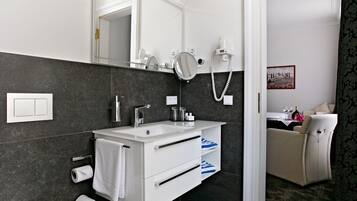 Un baño moderno con tocador blanco, paredes de baldosas oscuras, un espejo grande, un secador de pelo y un perchero para toallas.