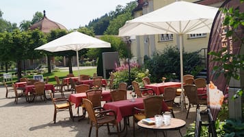 An outdoor dining area with tables and chairs, umbrellas, and a building in the background.