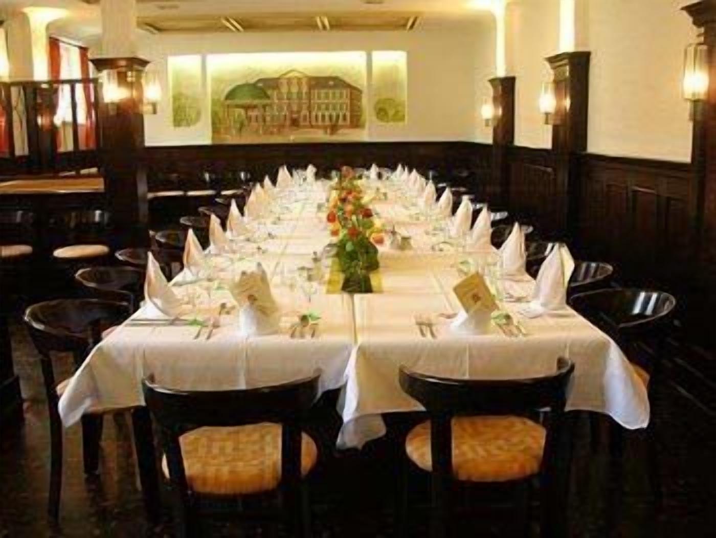 A formal dining room with a long table set for a meal, surrounded by chairs.