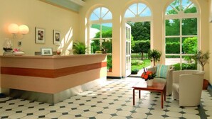 A reception area with a glass ceiling, a reception desk, and a seating area with a view of the outdoors. - Badhotel Bad Brückenau (Bad Brueckenau)