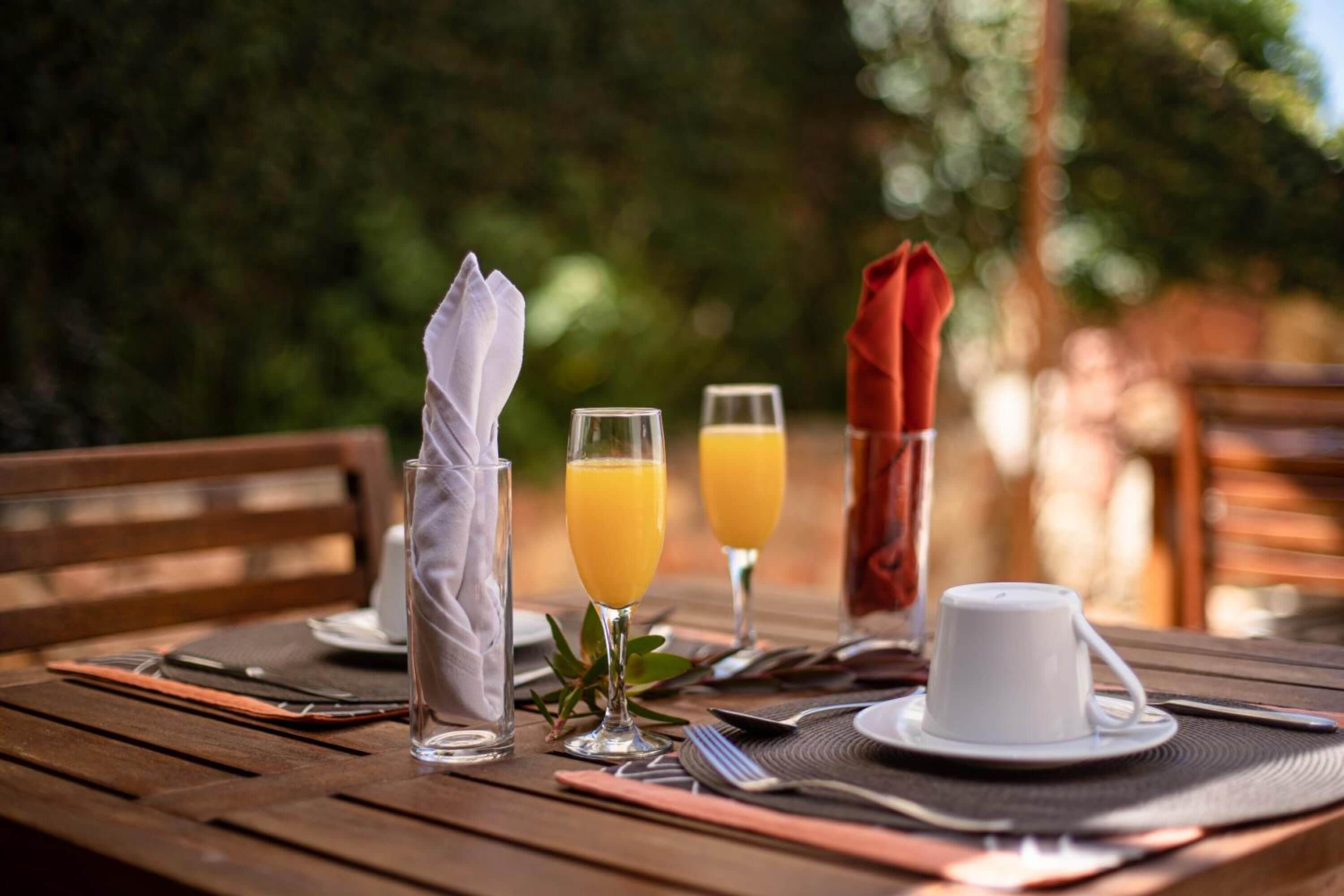 A wooden dining table set with a white cup, two glasses of orange juice, and a napkin.