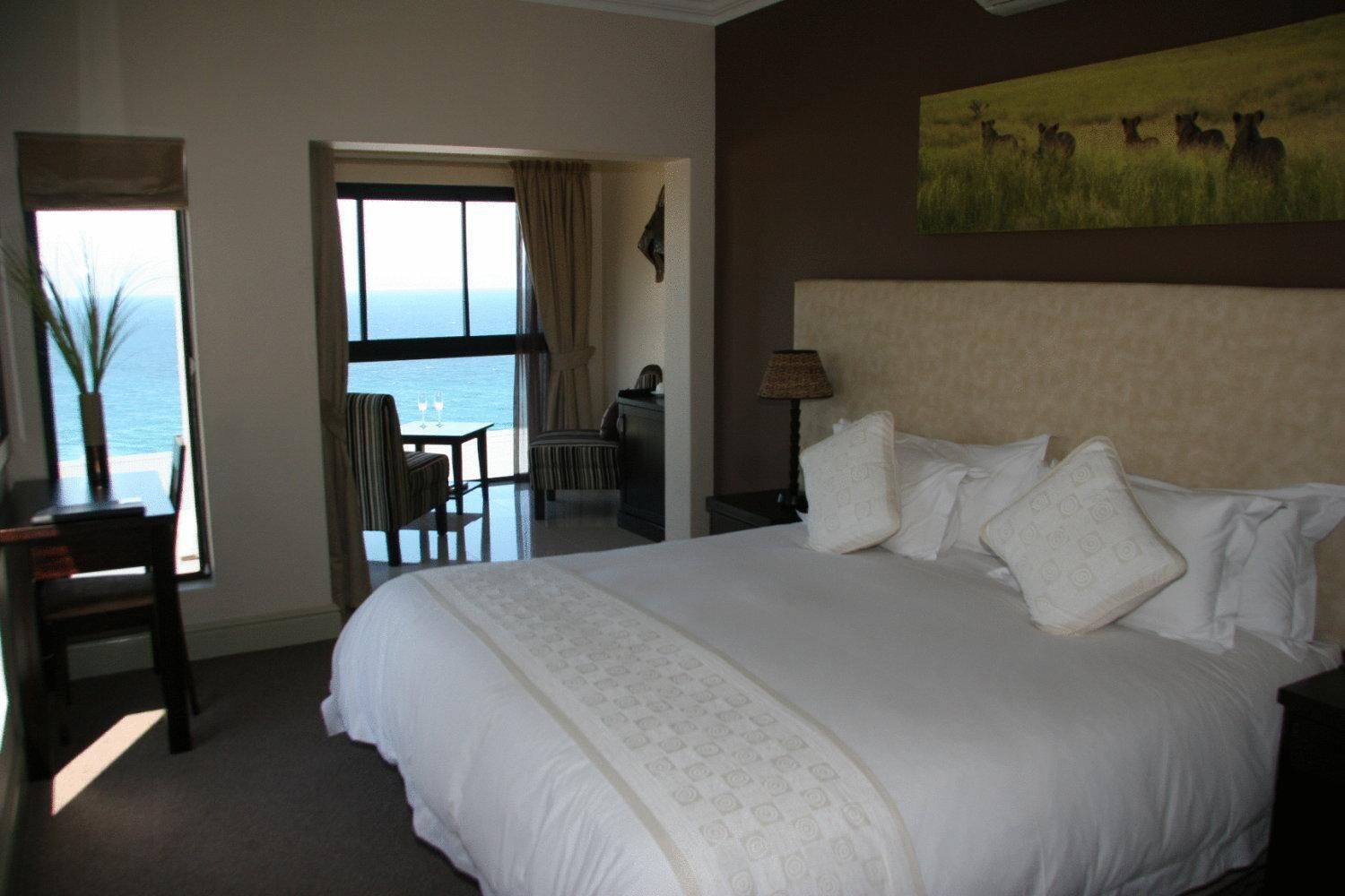 A hotel room with a large bed, a desk, a chair, and a view of the sea through a window.