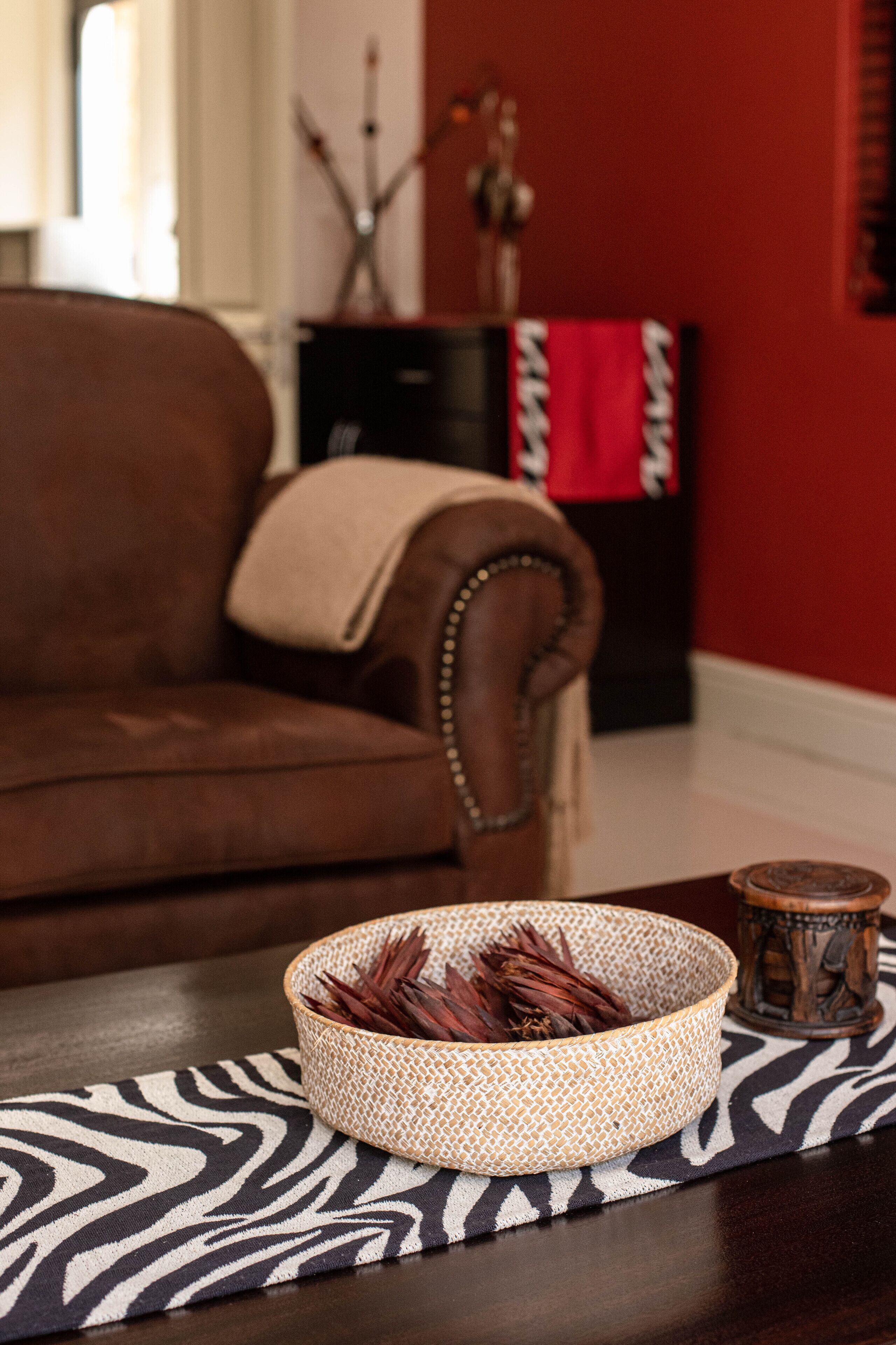 Un canapé en cuir marron avec un plaid, un panier tressé posé sur un tapis à motifs zébrés et un petit objet décoratif sur une table en bois.