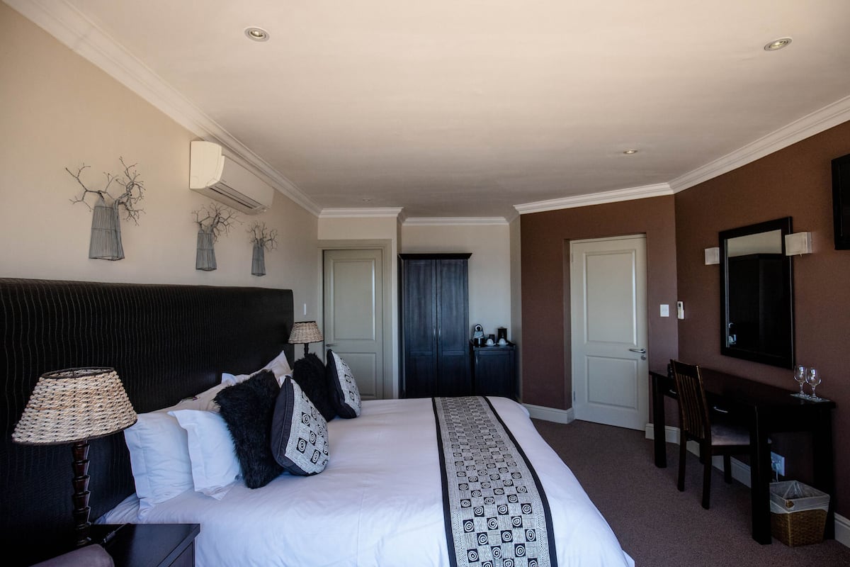 A hotel room with a large bed, a desk, a chair, and a mirror.