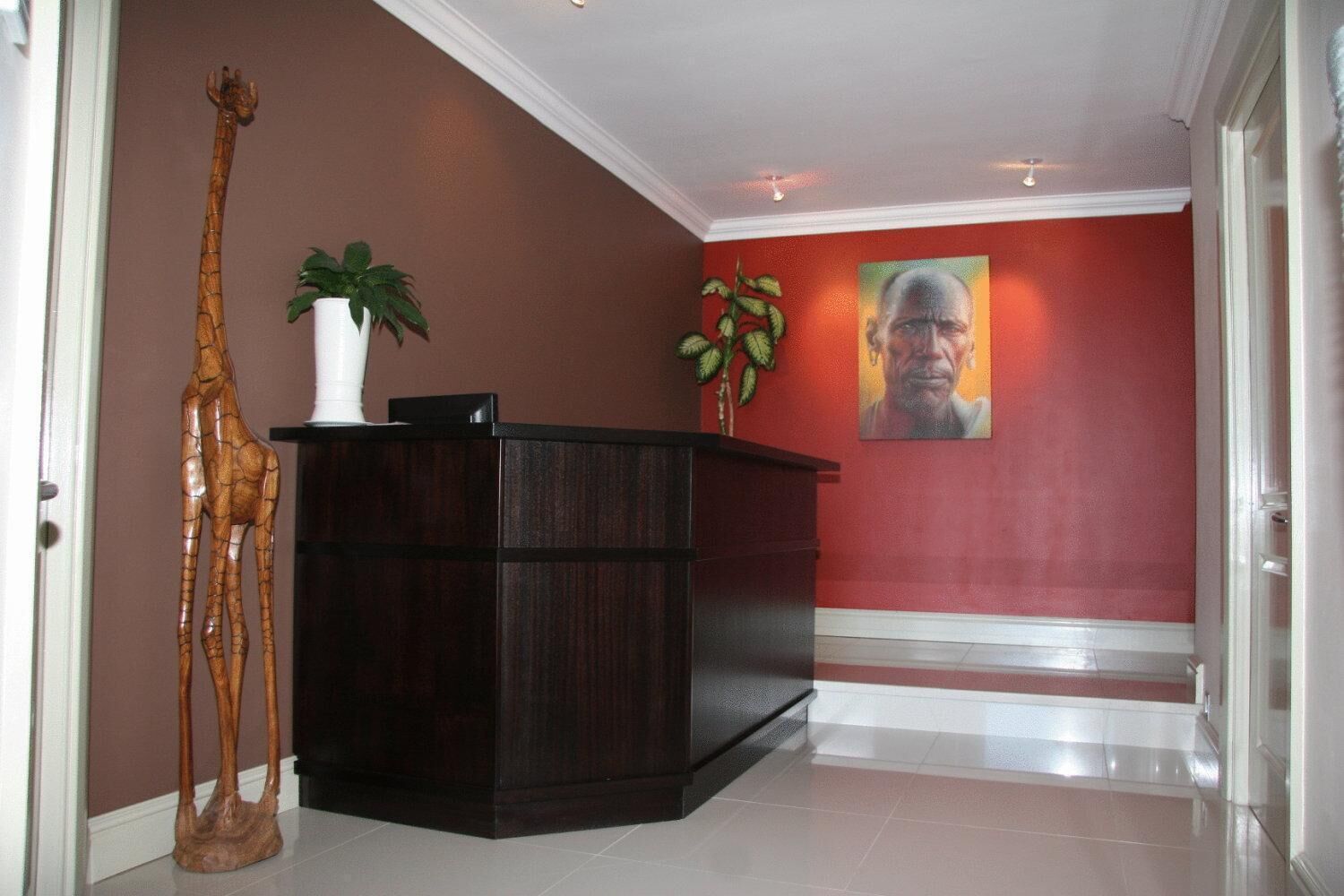 A hallway with a wooden giraffe sculpture, a dark wooden desk, and a red wall with a portrait.