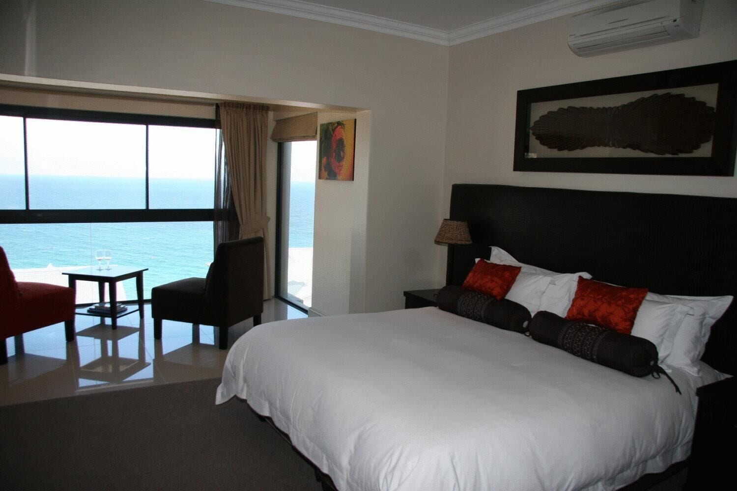 Habitación de hotel con una cama grande, vistas al mar y un comedor con mesa y sillas.