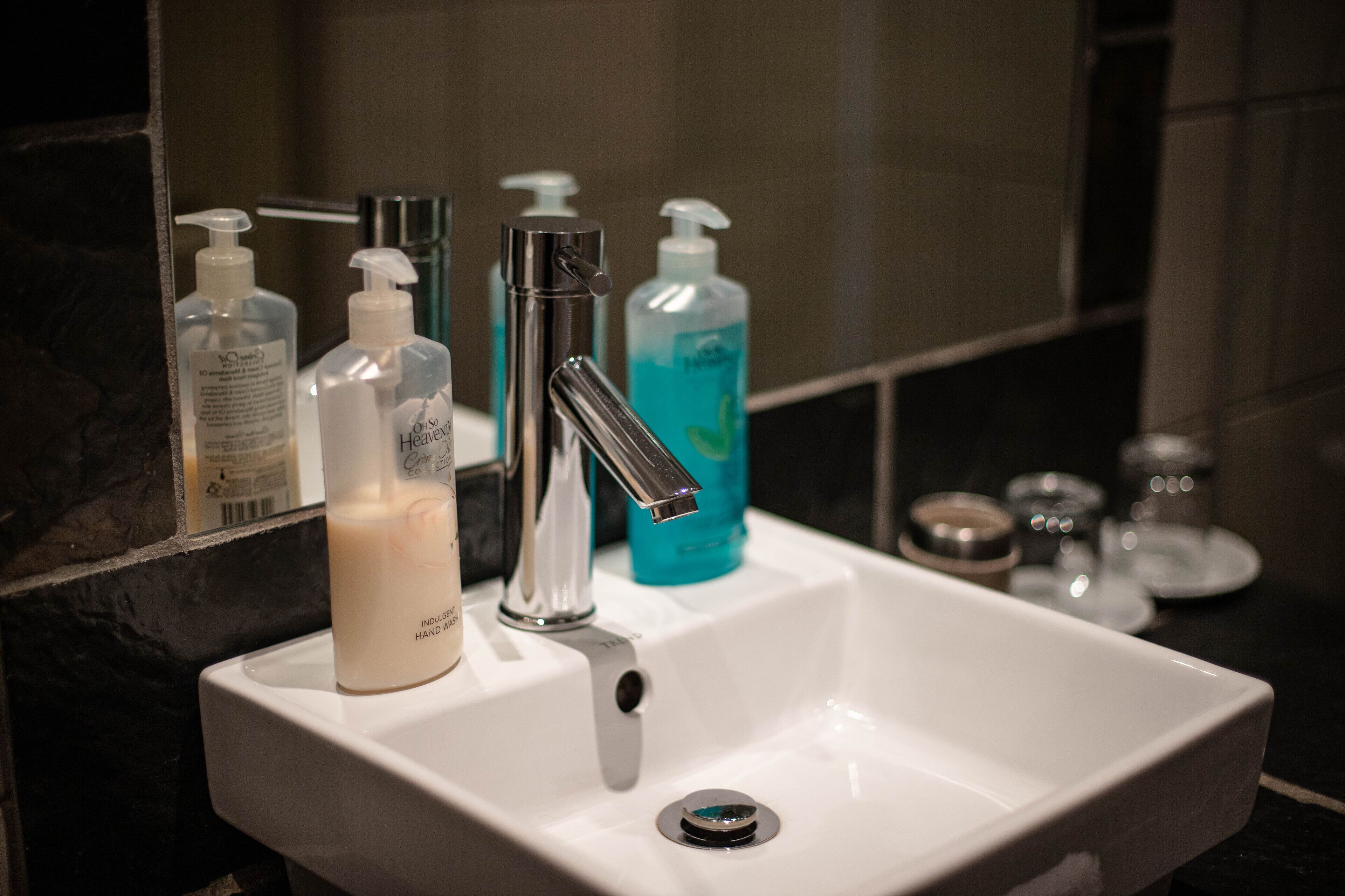 A bathroom sink with a mirror, a faucet, and several bottles of hand soap.