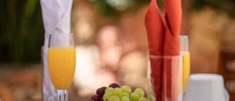 A table set with a glass of orange juice, a bowl of grapes, and a glass with red napkins.