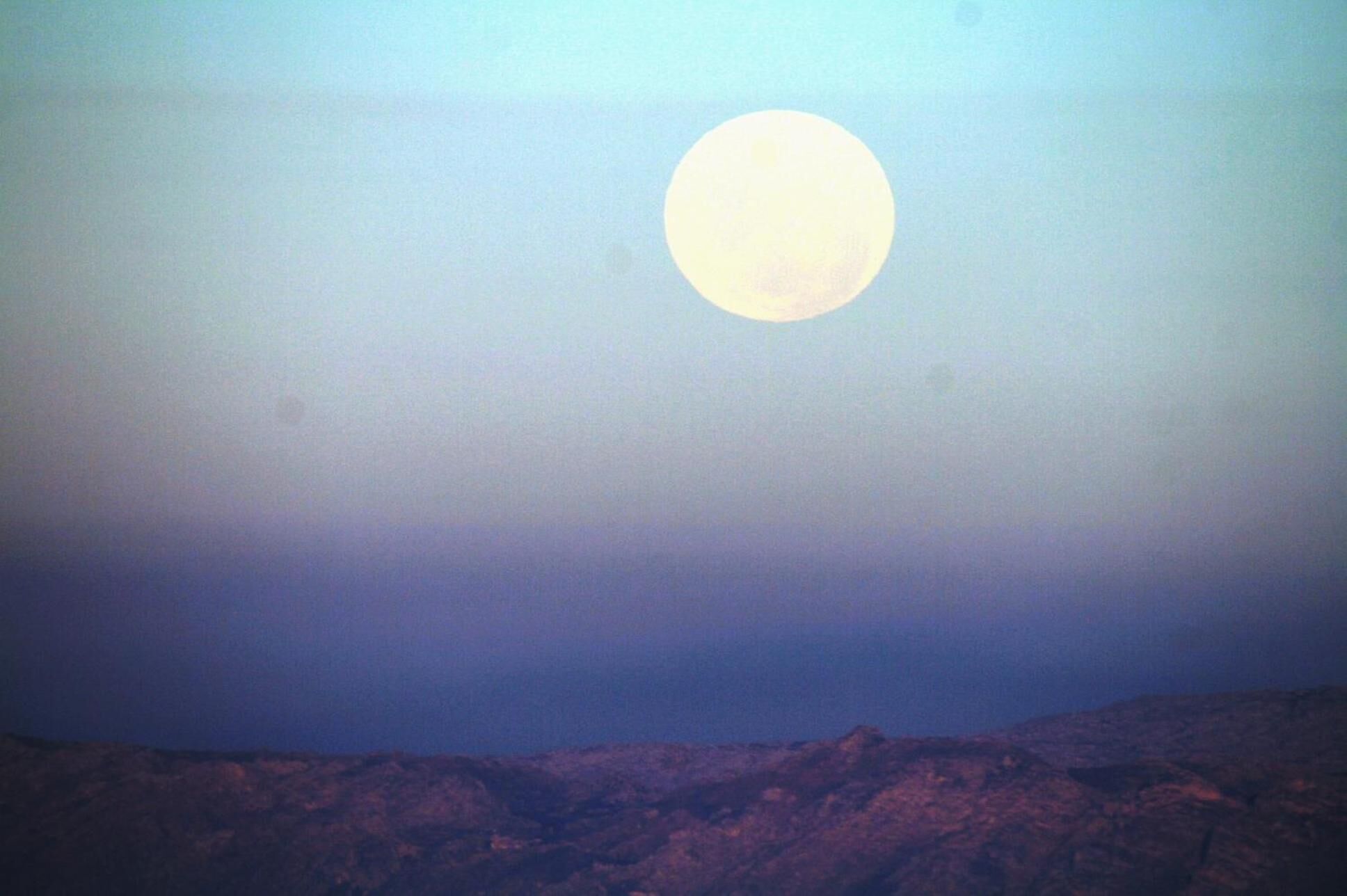 A landscape with a large moon in the sky and rocky terrain below.