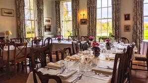 A dining room with multiple tables set for a meal, large windows with curtains, and framed pictures on the walls. - Warwick Hall (Carlisle)