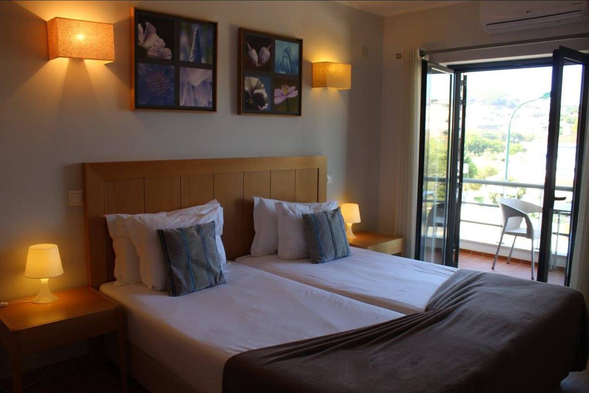 Une chambre d’hôtel avec deux lits, une tête de lit en bois, des lampes fixées au mur et un balcon avec une chaise.