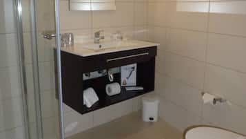 A bathroom with a glass shower enclosure, a white sink with a dark countertop, and a white toilet.