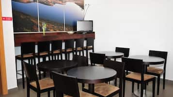 Un comedor con mesas y sillas redondas, un televisor sobre una encimera de madera y un cartel grande con un paisaje en la pared.