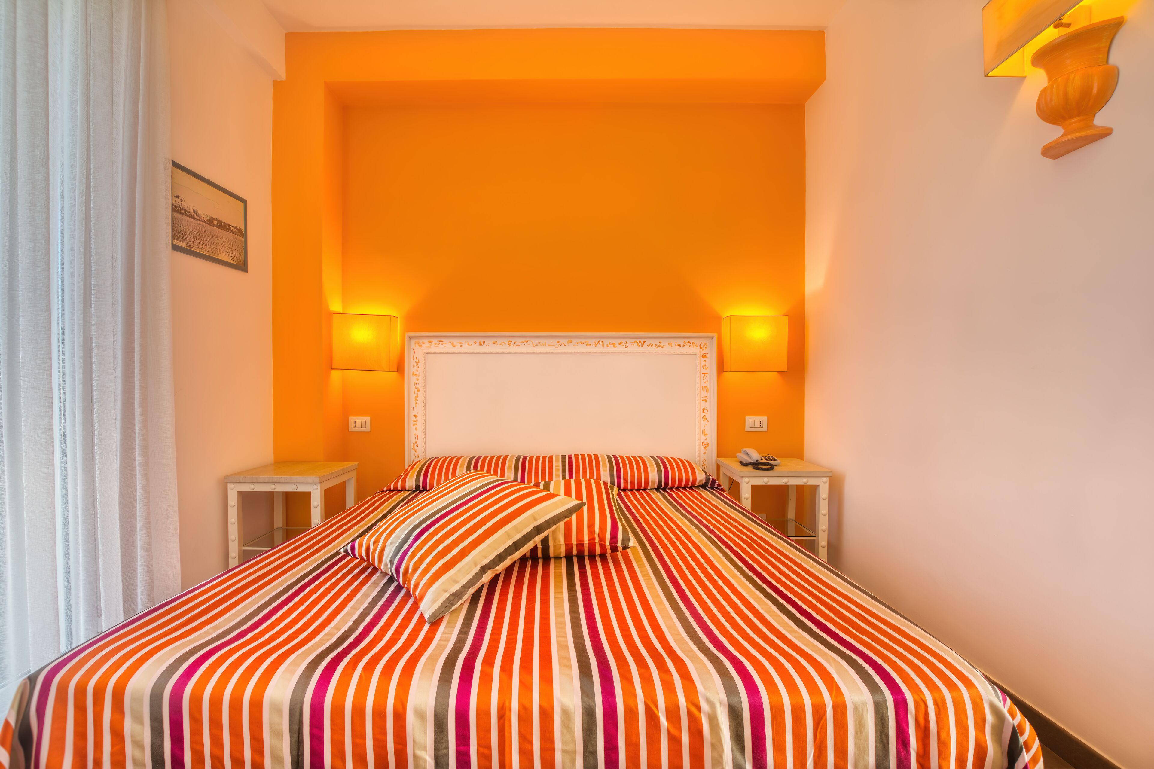 Habitación de hotel con una cama grande, dos mesitas de noche y un cabecero con lámparas fijadas a la pared.