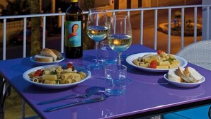 A table set with dinner plates, glasses, and a bottle on a balcony overlooking a cityscape at dusk. - Hotel O'scià (Lampedusa)