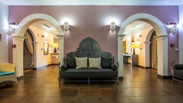 A lobby with a central sofa, archways, and wall sconces.