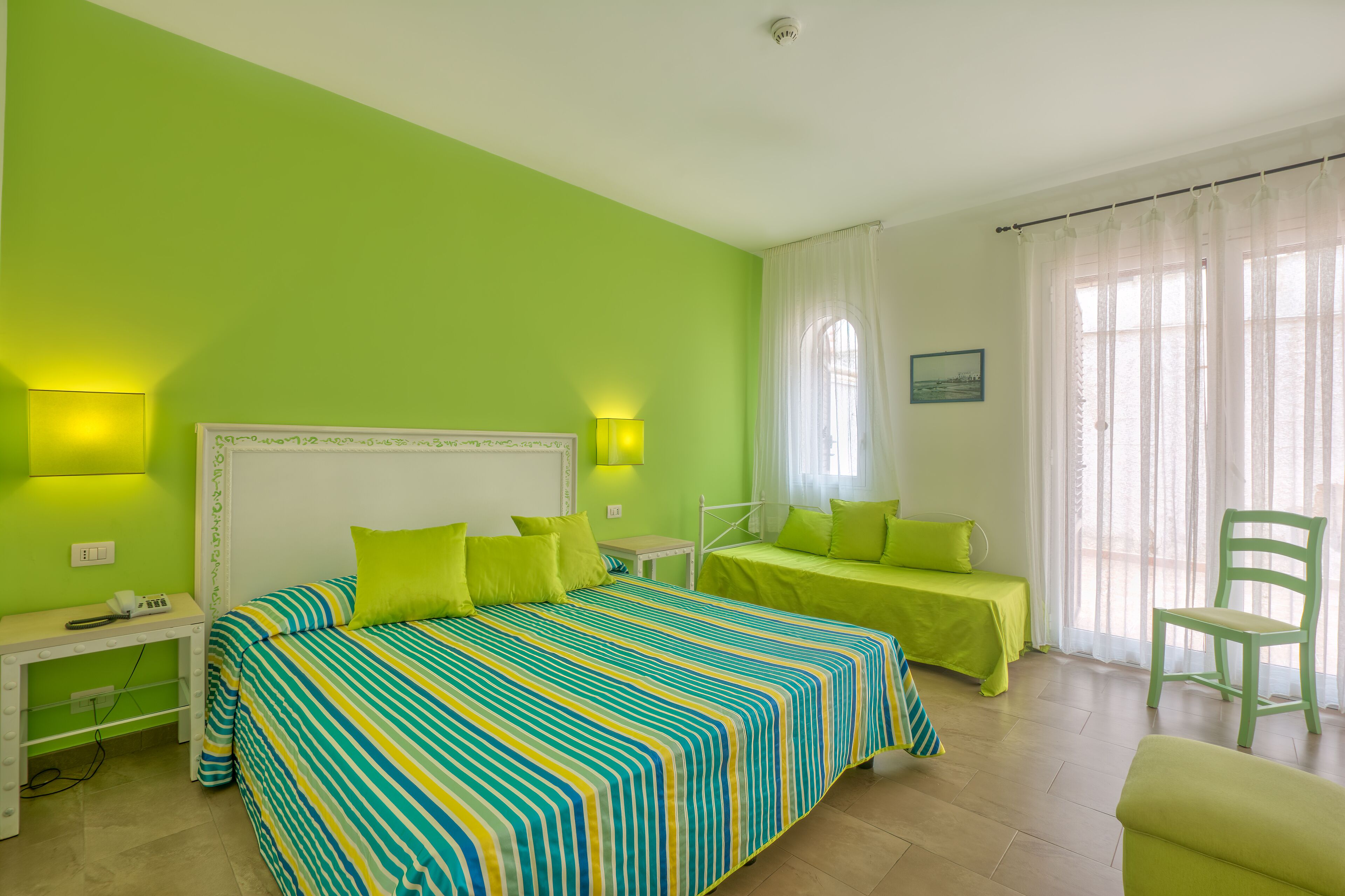 A room with a large bed, two bedside tables, a chair, and a window with curtains.