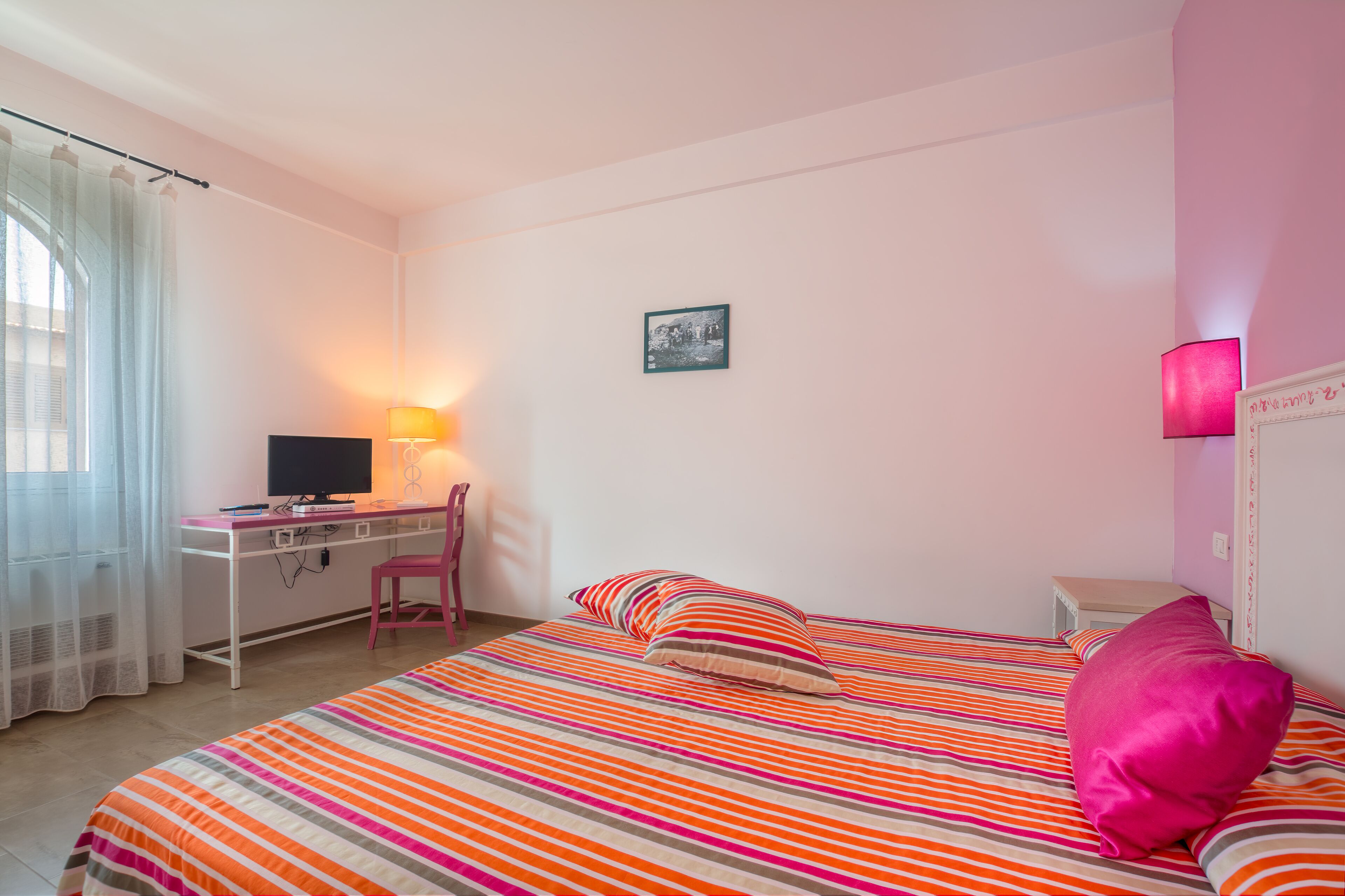 Un dormitorio con cama, escritorio, silla, televisor y lámpara.