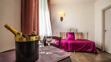 Une chambre avec un lit, une table de chevet sur laquelle se trouvent une bouteille et des verres, une lampe et une fenêtre avec des rideaux.