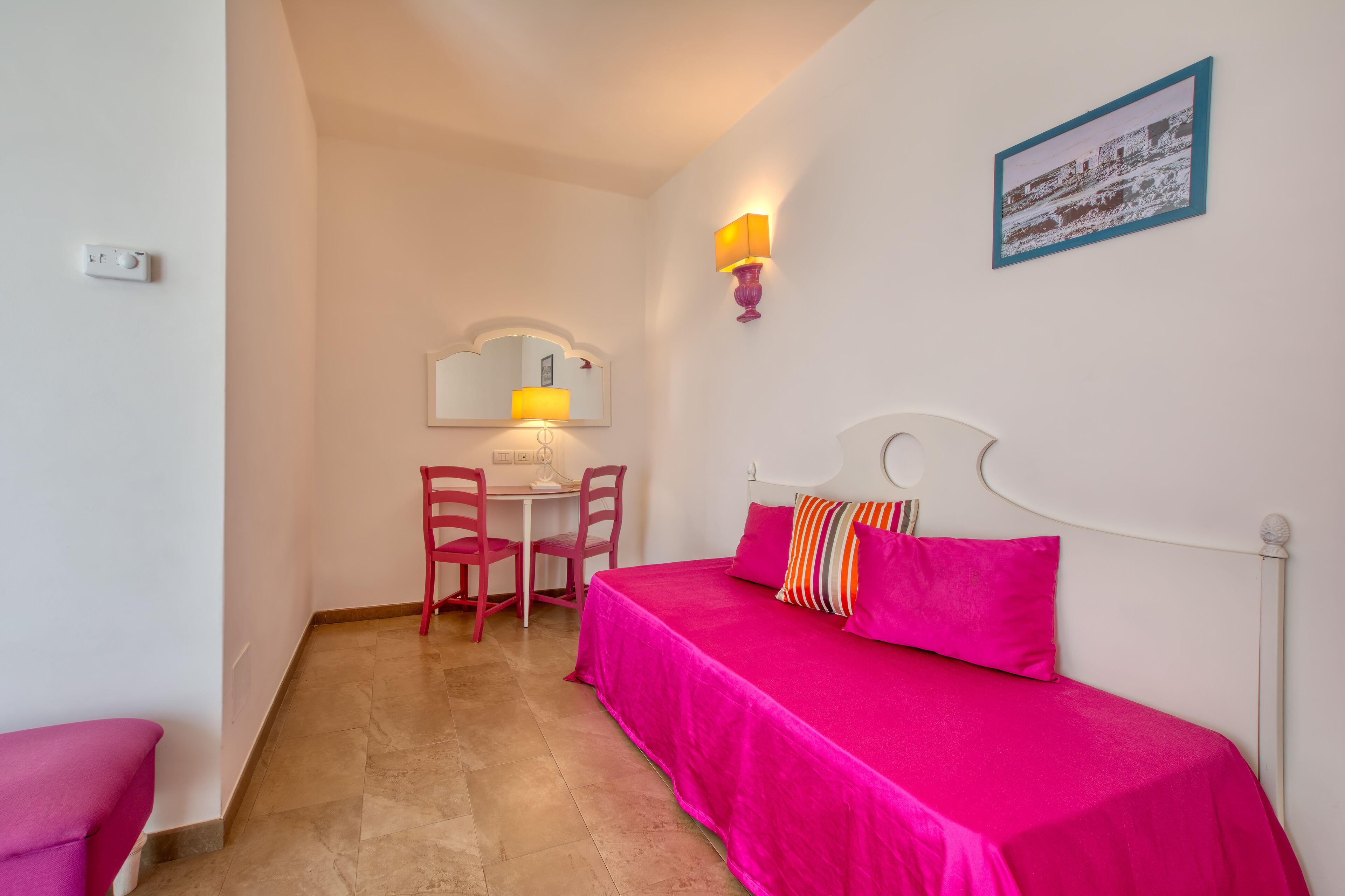 A small, bright room with a bed, a desk, and a chair.
