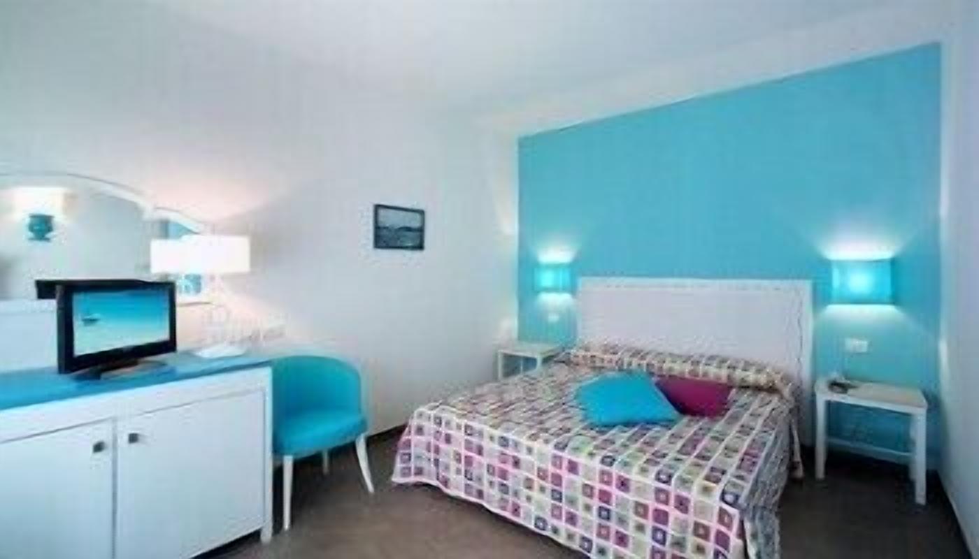 A bedroom with a bed, a desk with a computer, a chair, and bedside lamps.