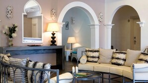 A living room with a sofa, armchairs, a coffee table, and a fireplace. There are two lamps on side tables, and a mirror above the fireplace. - Hotel O'scià (Lampedusa)