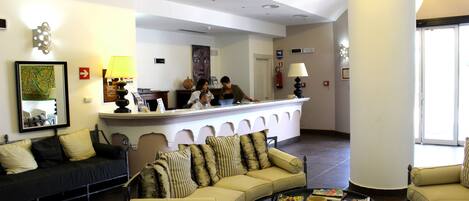 Um saguão de hotel com balcão de recepção, sofás e mesa de centro.