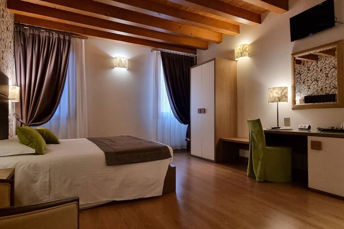 A hotel room with a bed, a desk, a chair, and a mirror.