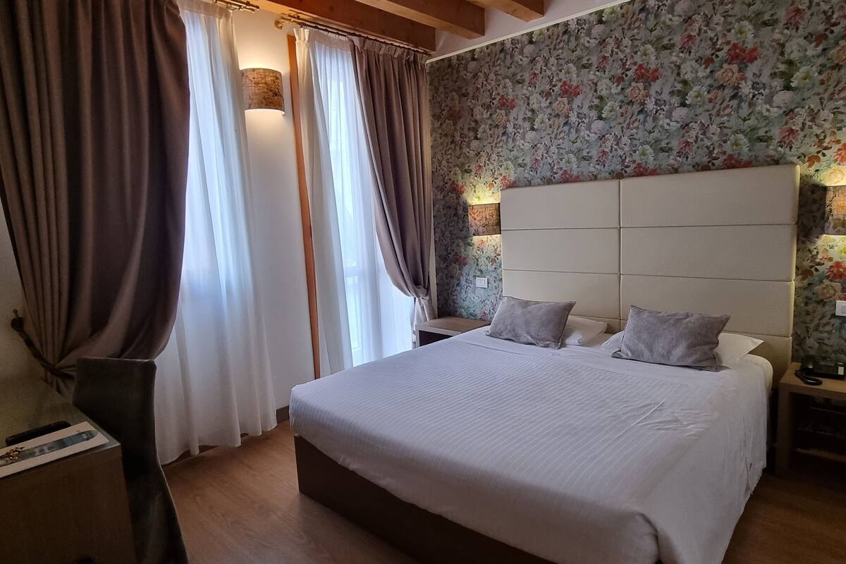 A hotel room with a large bed, two bedside tables, a lamp, and a floral wallpaper.