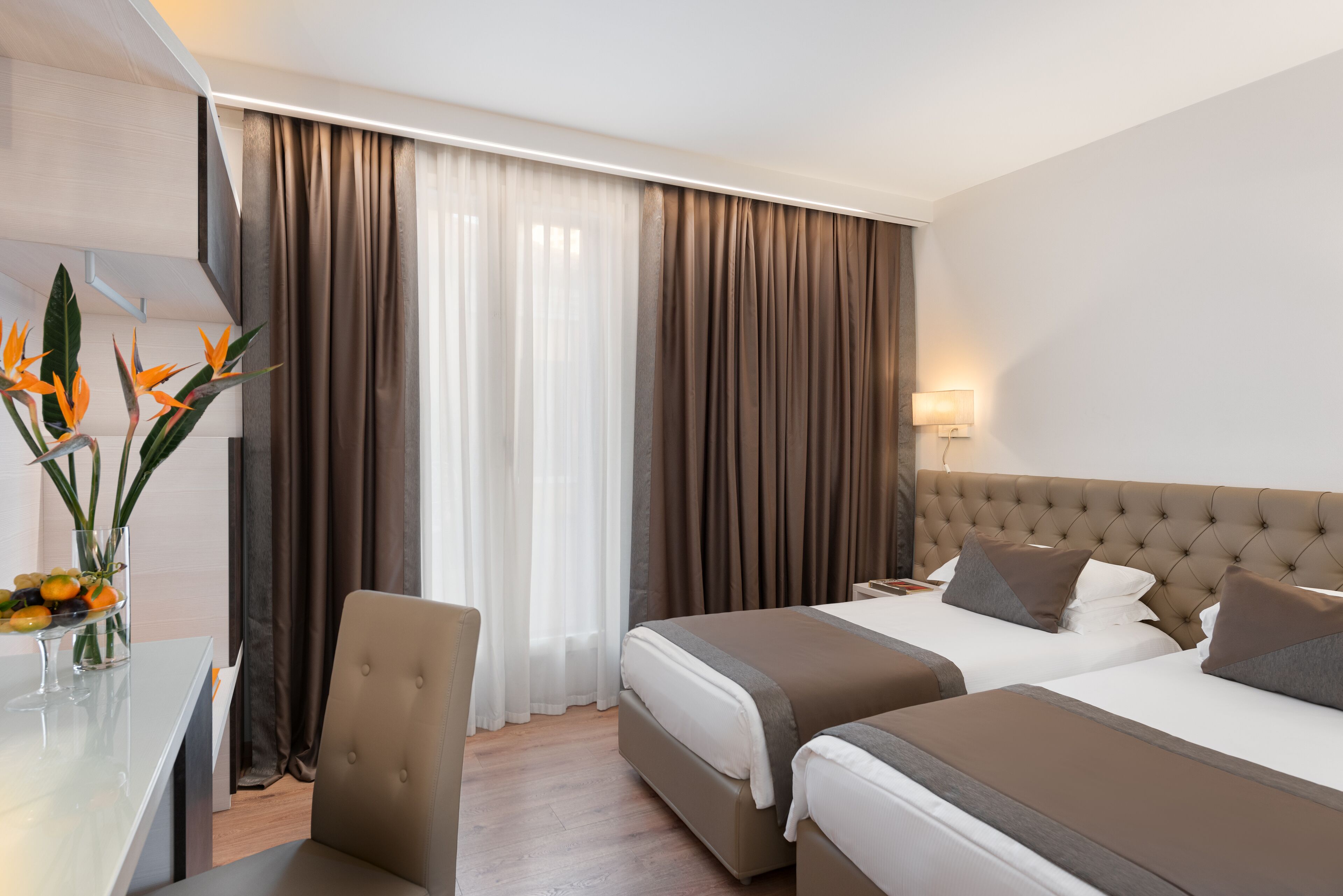 A hotel room with two beds, a desk, and a chair.