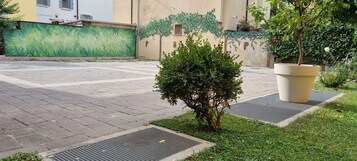 Un cortile lastricato con un piccolo albero, un vaso grande e un muro decorato con un murale verde.