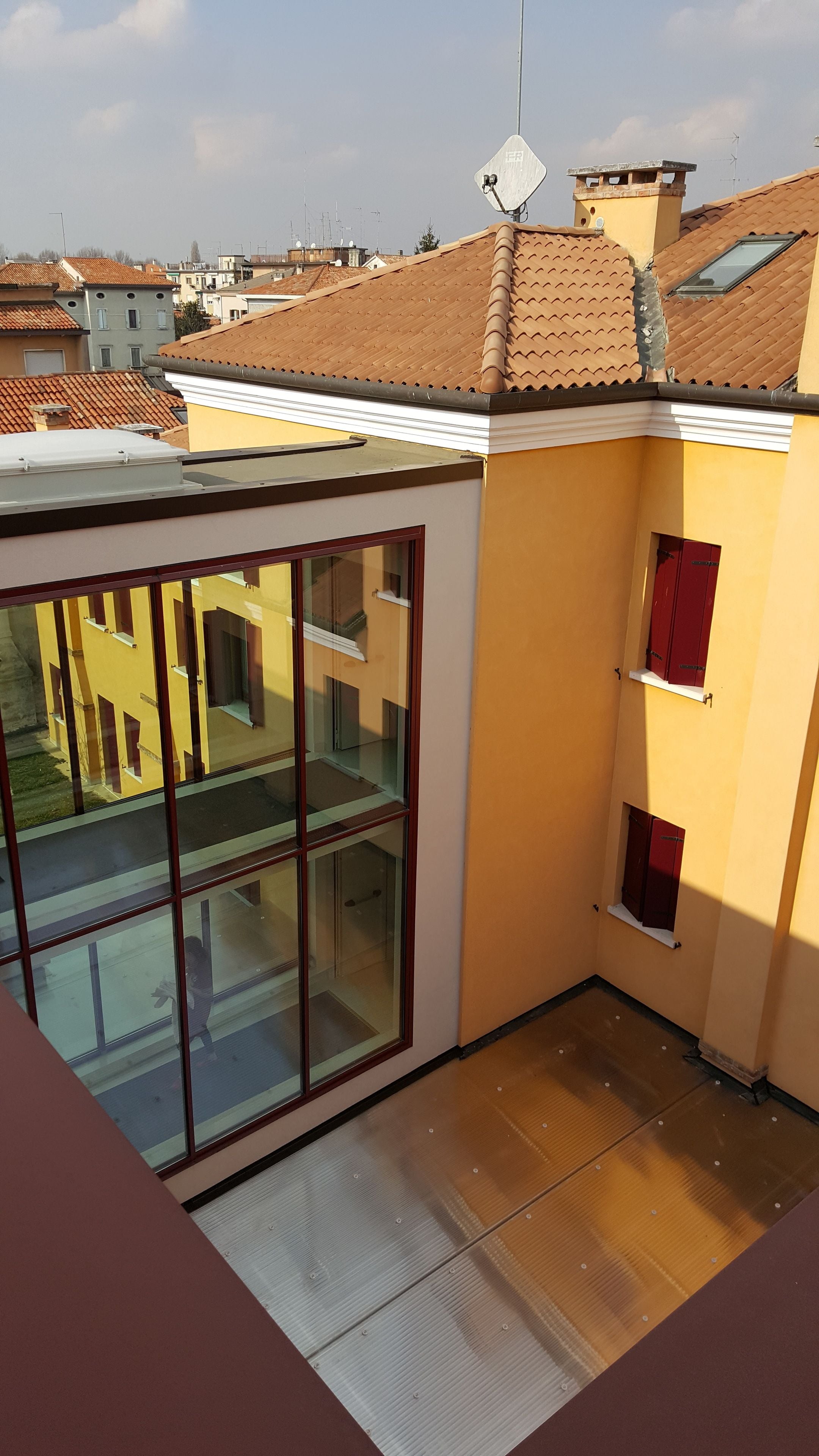 A balcony with a glass enclosure, a yellow wall, and a red door.
